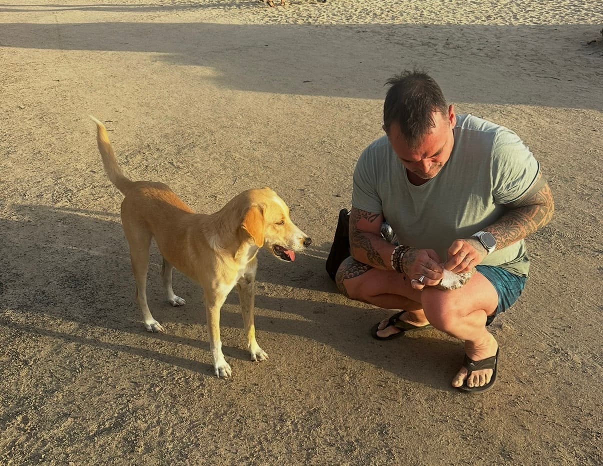 Een hondenprofessional zit gehurkt naast een rustige hond in de avondzon